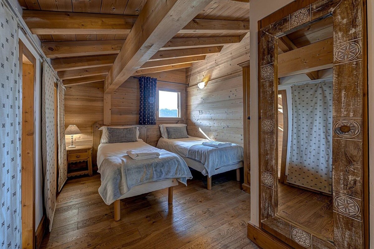 Cozy, all-wood cabin bedroom with two twin beds, a window, a bedside lamp, and a large rustic mirror.