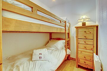 A bunk bed in a bedroom with a dresser and a lamp