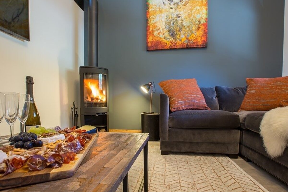 Cozy living room featuring a lit fireplace, a grey sofa with orange pillows, and a charcuterie board on a wooden coffee table.