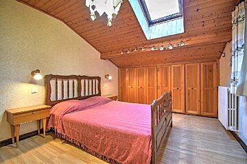 A cozy attic bedroom with a slanted wooden ceiling, skylight, wooden furniture, and a pink bedspread.