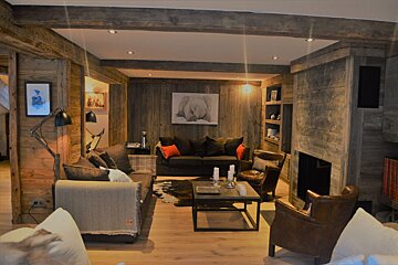Cozy, wood-clad living room features sofas, leather armchairs, a coffee table, fireplace, and an elephant painting on a paneled wall.