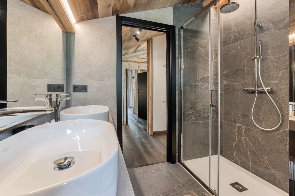 Modern bathroom with stone-tile walls, double vessel sinks, and a glass-enclosed walk-in shower.