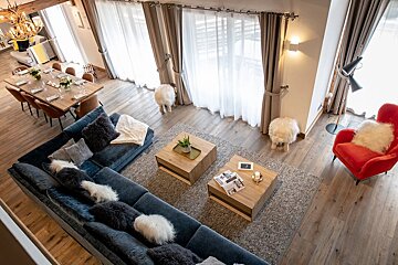 Overhead view of a modern, cozy living and dining room with a large blue sectional, red armchair, wooden dining table, and big windows.