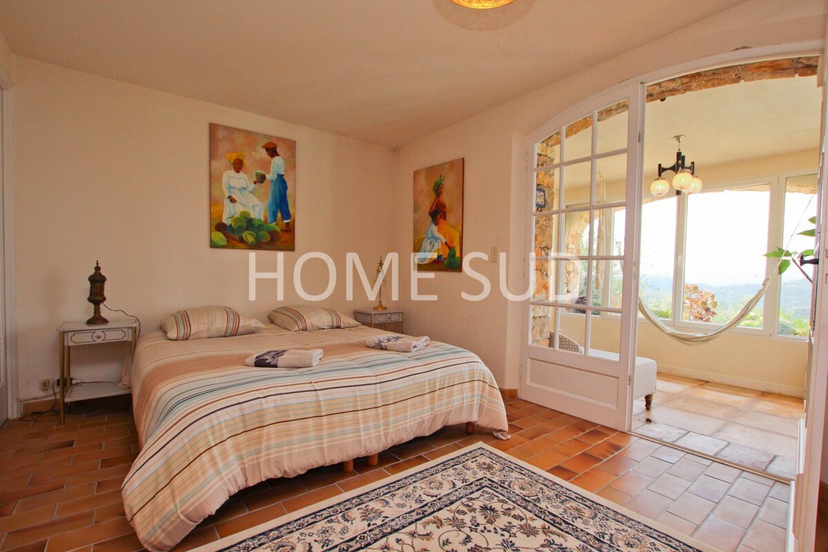 A cozy bedroom with a striped bed, terracotta floor, and artwork, leading to a bright sunroom with a hammock and outdoor views.