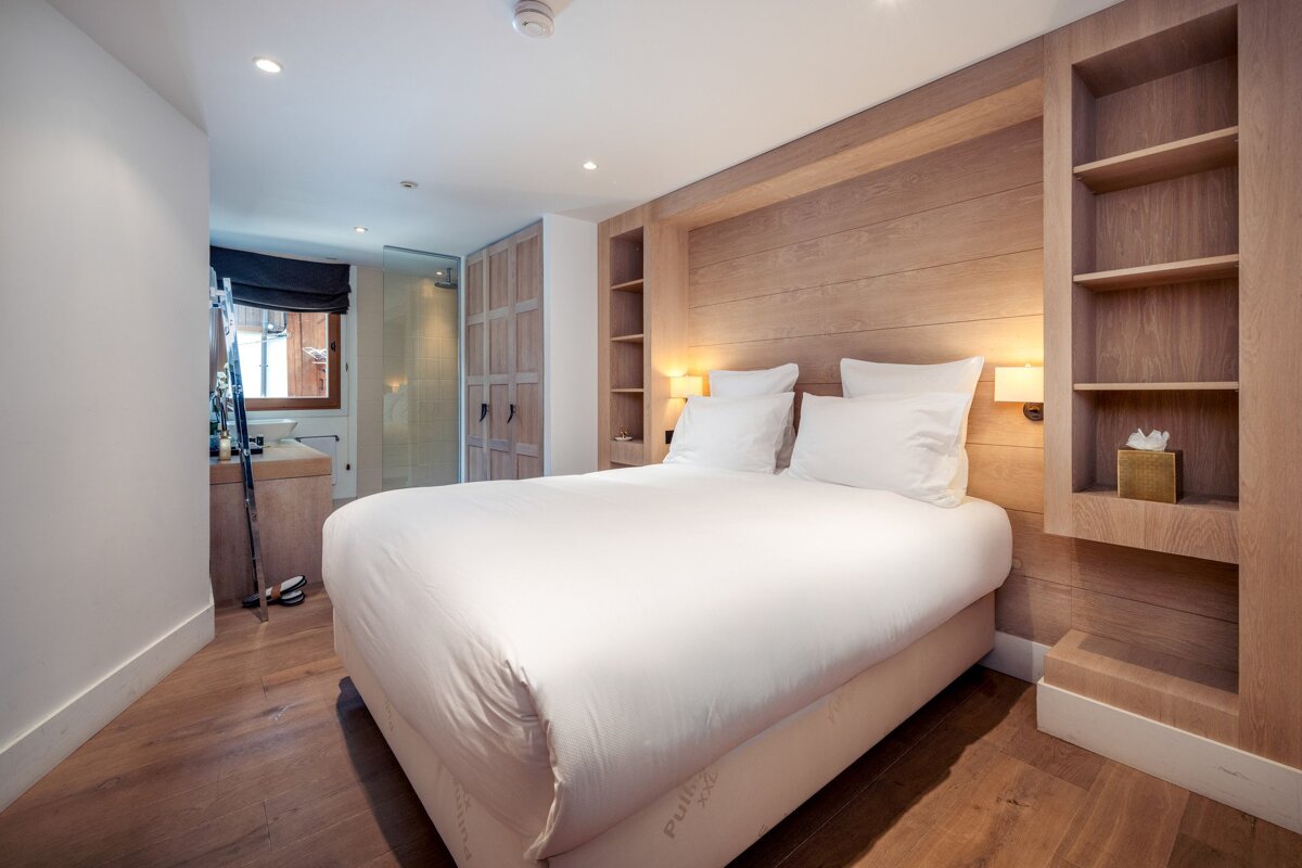 Modern bedroom featuring a double bed with white linens, built-in wood shelving, and a wooden floor.