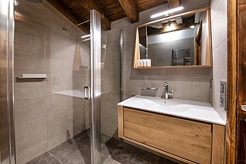 Modern rustic bathroom with a glass shower stall, a floating wooden vanity, and a large framed mirror beneath exposed ceiling beams.
