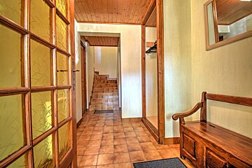 Rustic home entryway featuring tiled flooring, a wooden bench, a glass-paned door, and stairs in the background.