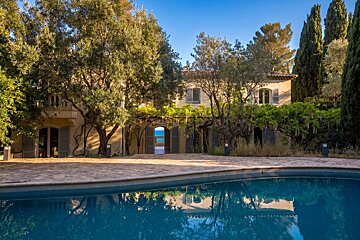 A luxury villa with a swimming pool reflecting trees, featuring a view of the blue sea through an open archway.