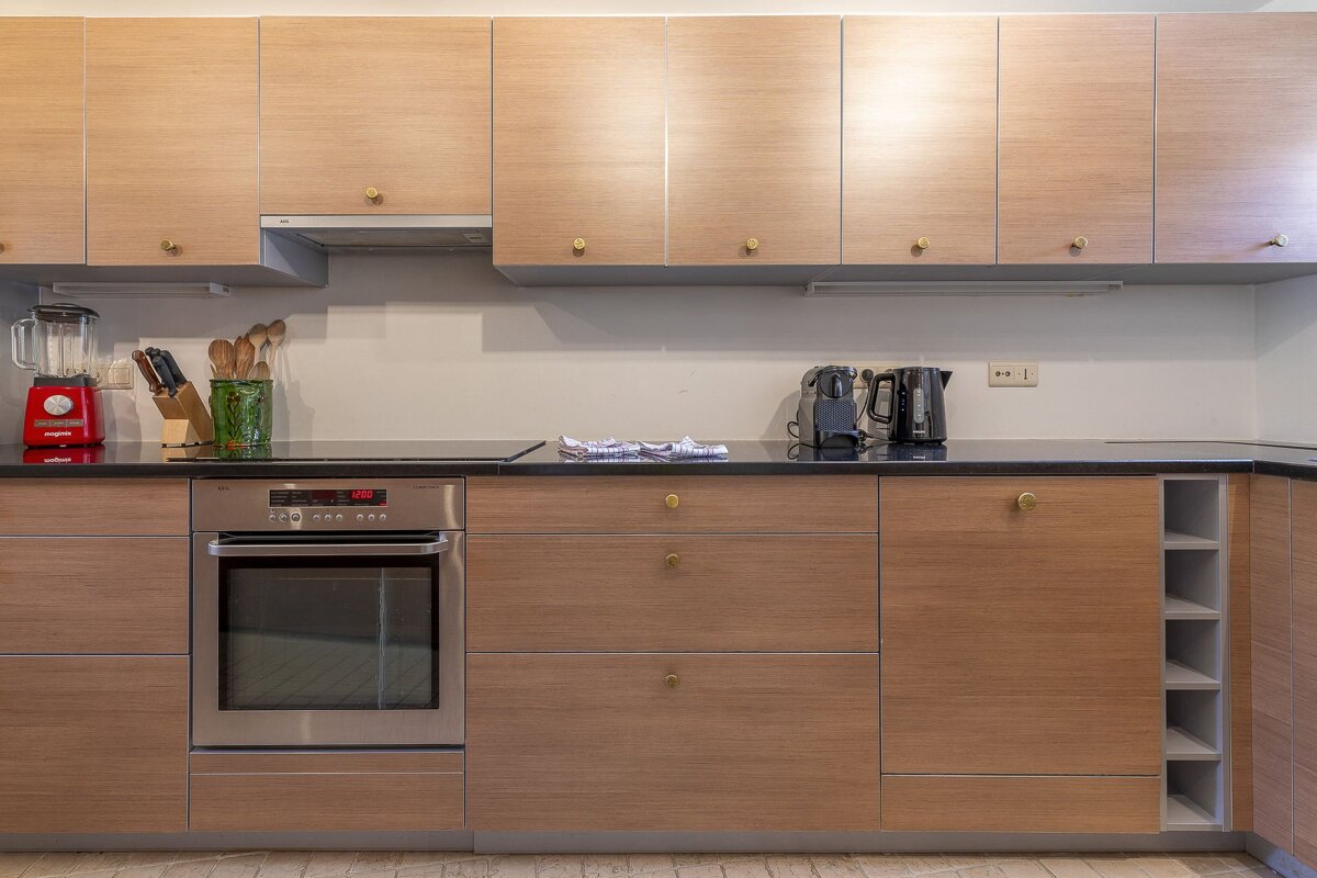 Modern kitchen featuring light wood cabinets, a black countertop, an integrated oven, and countertop appliances like a red blender.