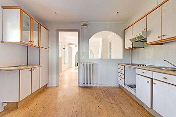 An empty kitchen with wooden floors and white cabinets