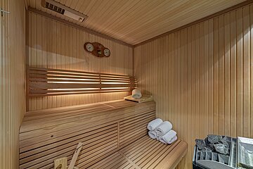 A light wooden sauna interior with multi-level benches, a heater with rocks, white towels, and wall gauges.