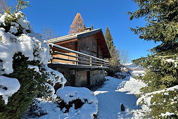 A rustic wooden cabin blanketed in snow, nestled among frosted trees under a clear blue winter sky.