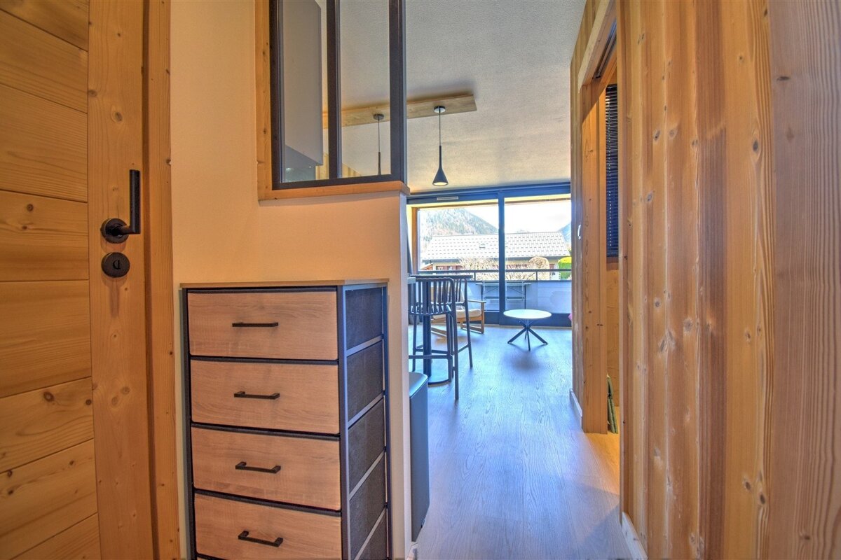 Modern chalet hallway with wood-paneled walls, a chest of drawers, and a view into a bright living room.