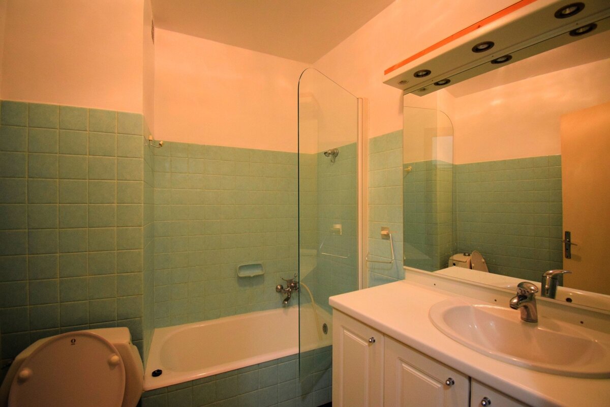 A bathroom with light green tiled walls, peach upper walls, a white bathtub, toilet, and a vanity with a sink and large mirror.