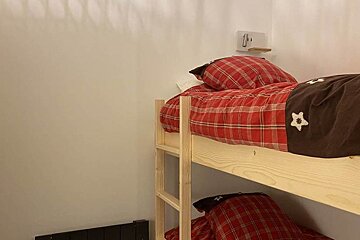 A bunk bed with red plaid sheets and brown pillows