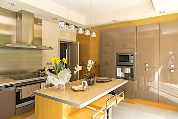A sleek, modern kitchen with stainless steel appliances, glossy beige cabinets, a light wooden island, and floral accents.