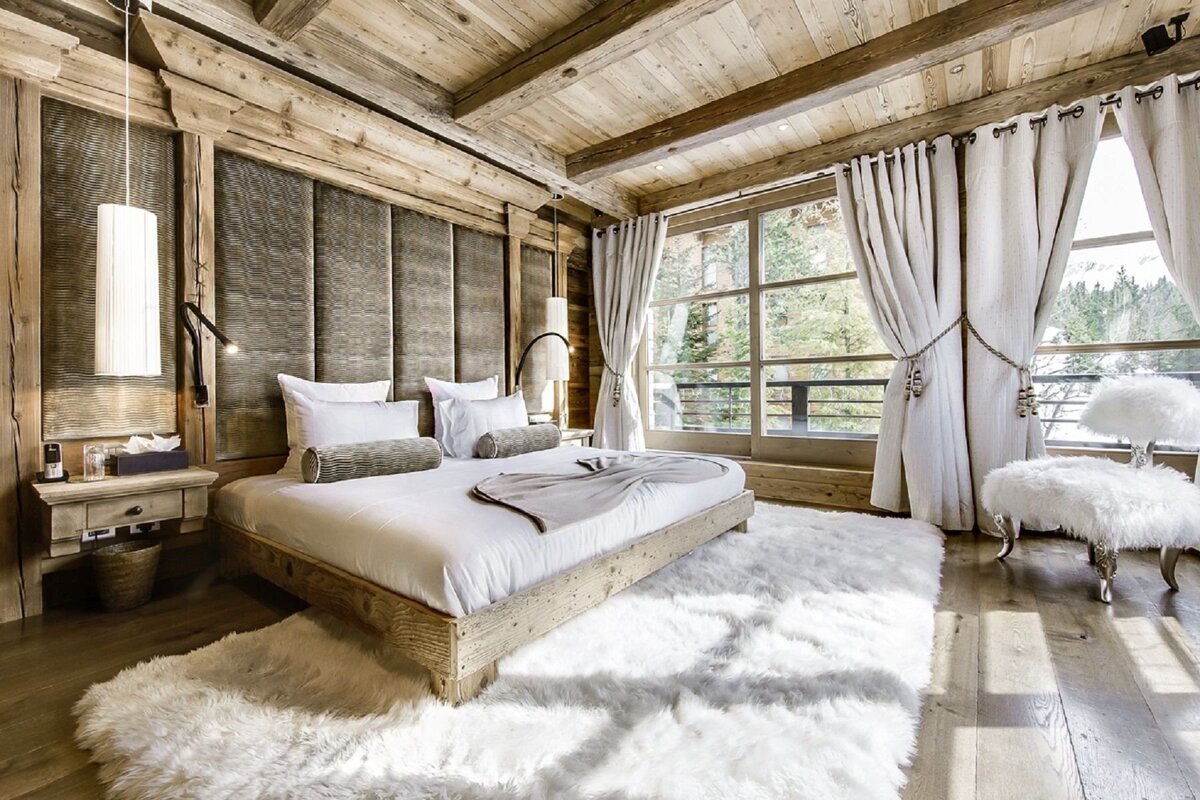 Luxurious, rustic wooden chalet bedroom with a large window view. Features a plush white bed, fluffy rug, and cozy, inviting ambiance.