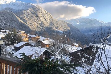 A charming, snow-covered mountain village basks in sunlight, with wooden chalets nestled against vast, white peaks on a bright winter's day.