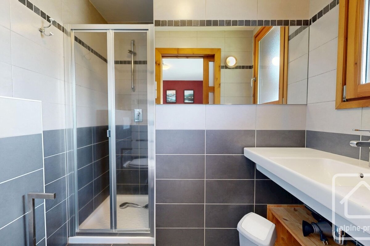 Modern bathroom with white and gray tiling, a glass-door walk-in shower, a large mirror, and a white sink.