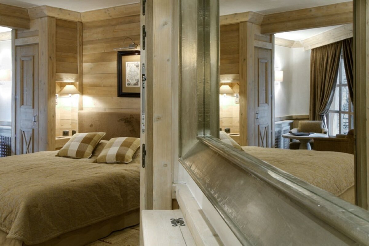 Cozy, rustic wood-paneled bedroom with a large bed, checkered pillows, and a mirror reflecting a window area.