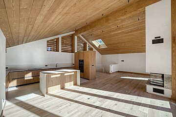 Bright, modern kitchen in an attic space, featuring light wood floors, ceiling, and cabinetry, illuminated by sunlight through a skylight and windows.
