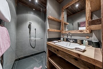 Rustic-modern bathroom featuring grey tile walls, a glass walk-in shower, and a wooden sink vanity with a matching framed mirror.