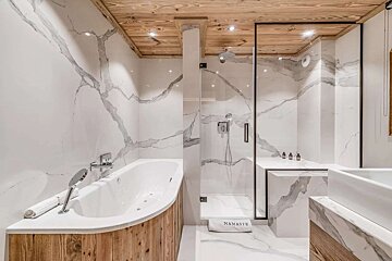 Elegant bathroom with white veined marble walls/floor, warm wooden ceiling, modern glass shower, and a curved bathtub with wood trim.
