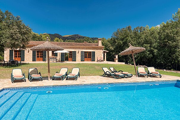 A swimming pool with chairs and umbrellas in front of a house