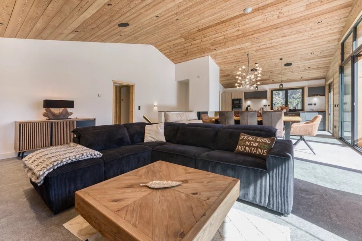 Cozy rustic-modern living room featuring a dark sectional sofa, wooden coffee table, and vaulted wood plank ceiling.