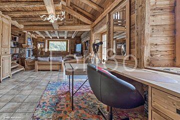 Rustic wooden chalet interior featuring a desk with a colorful rug and a cozy living area in the background.