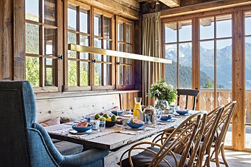 A dining room with a table and chairs and mountains in the background