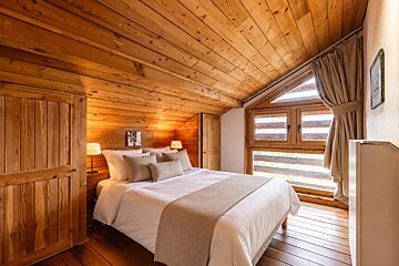 Cozy cabin attic bedroom with warm wood paneling, a neatly made bed, and a large window.
