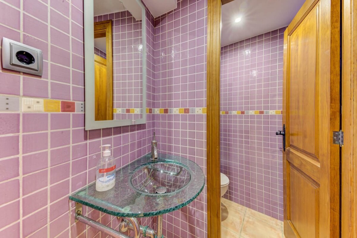 A bathroom with purple tiles and a glass sink