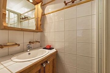 A bathroom with white tiles and a sink and mirror