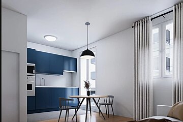 A modern apartment featuring a dark blue kitchen and a small wooden dining table under a black pendant light.