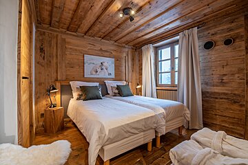 Cozy, rustic bedroom featuring two single beds, complete wood paneling, a snowy window view, and a polar bear print.
