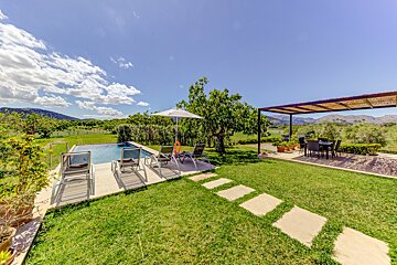 A swimming pool surrounded by chairs and umbrellas with mountains in the background