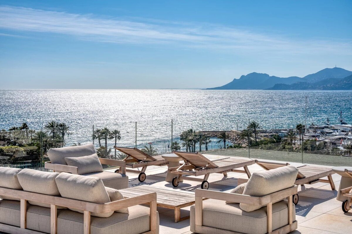 Luxurious rooftop terrace with comfortable lounge seating and sun loungers, offering a stunning, sunlit sea view with mountains.