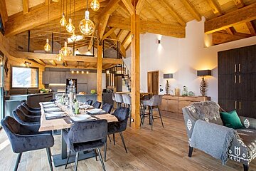 Luxurious chalet interior with exposed wooden beams, a dining table set for dinner, warm pendant lights, and a cozy seating area.