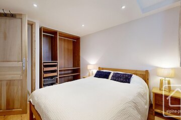 A cozy wooden bedroom with a white bed, open closet, nightstands, lamps, and a wooden door.