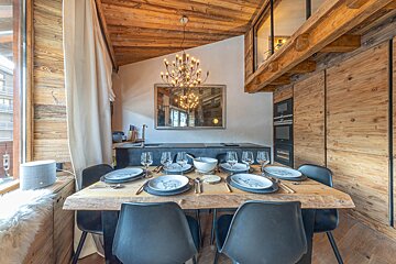 Cozy chalet dining area with a rustic wooden table set for six, black modern chairs, and a decorative branch chandelier.