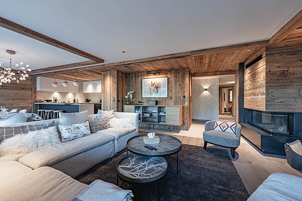 Cozy chalet living room with warm wood-paneled walls, a large sectional sofa, nested coffee tables, and a modern fireplace.