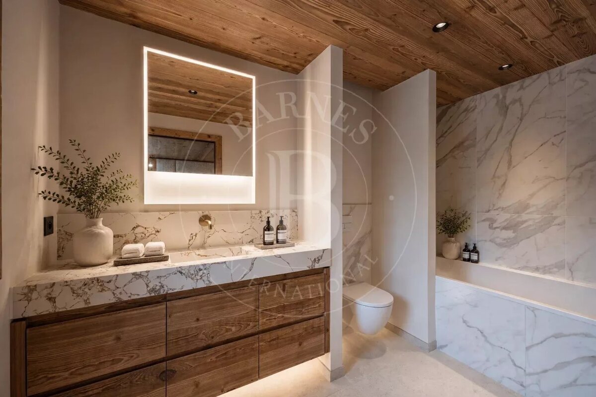 A modern bathroom featuring a marble vanity with a wooden cabinet, a lighted mirror, a wooden ceiling, a toilet, and a bathtub.