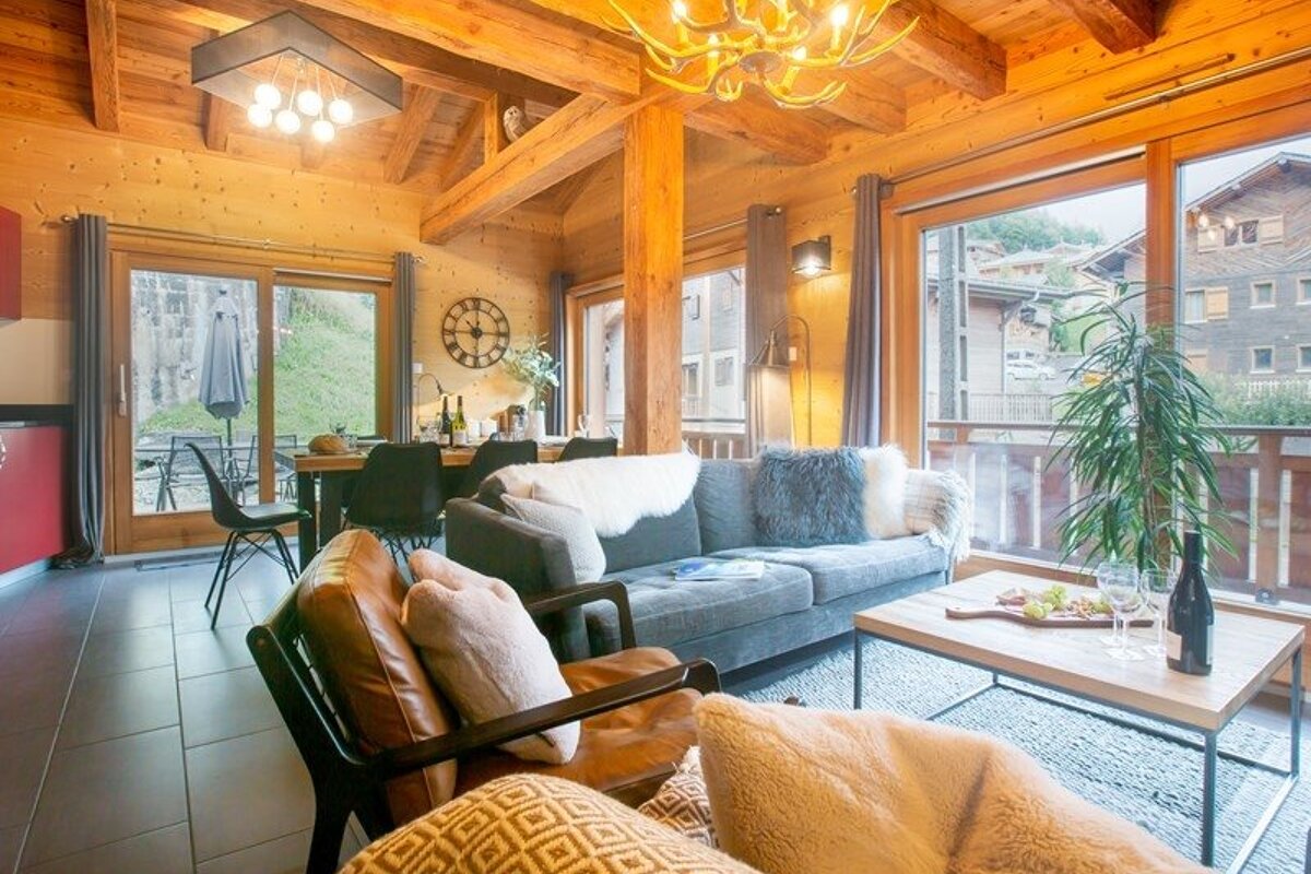 Cozy living room in a modern wooden chalet with plush sofas, rustic timber beams, a coffee table, and large scenic windows.