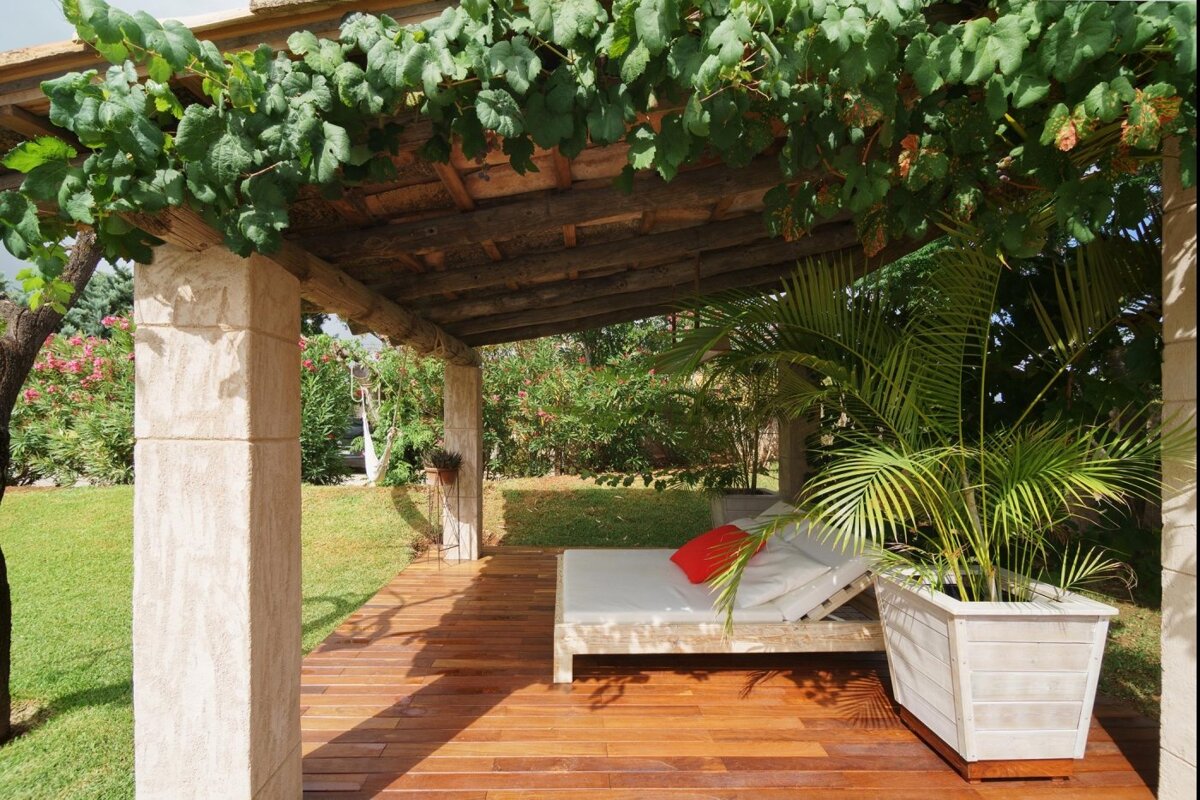 A wooden deck with a bed under a pergola