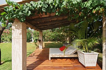 A wooden deck with a bed under a pergola