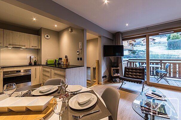 Modern open-plan apartment with kitchen, dining area, and living room leading to a balcony overlooking a snowy landscape.