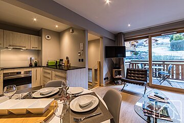 Modern open-plan apartment with kitchen, dining area, and living room leading to a balcony overlooking a snowy landscape.