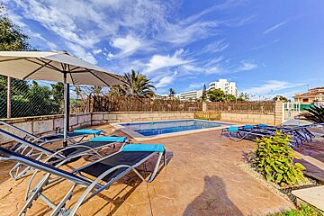 A swimming pool surrounded by chairs and a white umbrella