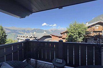View from a balcony overlooking a mountain village with chalets and distant peaks under a clear blue sky.